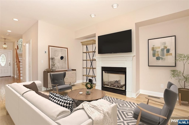 living area featuring a glass covered fireplace, baseboards, recessed lighting, wood finished floors, and stairs