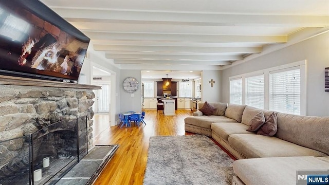 living area featuring light wood finished floors, a stone fireplace, and beam ceiling