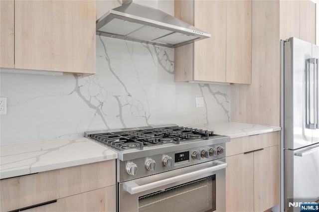 kitchen featuring wall chimney exhaust hood, light brown cabinetry, stainless steel appliances, and modern cabinets