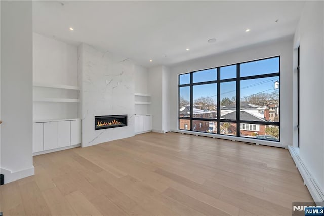 unfurnished living room featuring a baseboard heating unit, wood finished floors, built in shelves, and a high end fireplace