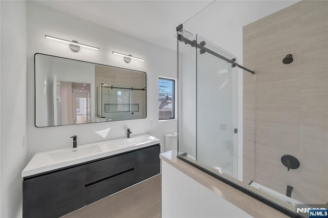 full bath with wood finished floors, a sink, double vanity, and tiled shower