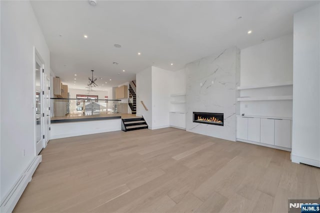 unfurnished living room with stairway, a baseboard radiator, light wood-style flooring, a premium fireplace, and recessed lighting