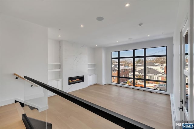 unfurnished living room with recessed lighting, wood finished floors, baseboards, a fireplace, and built in features