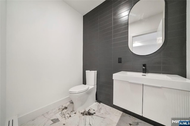 bathroom with toilet, tile walls, baseboards, marble finish floor, and vanity