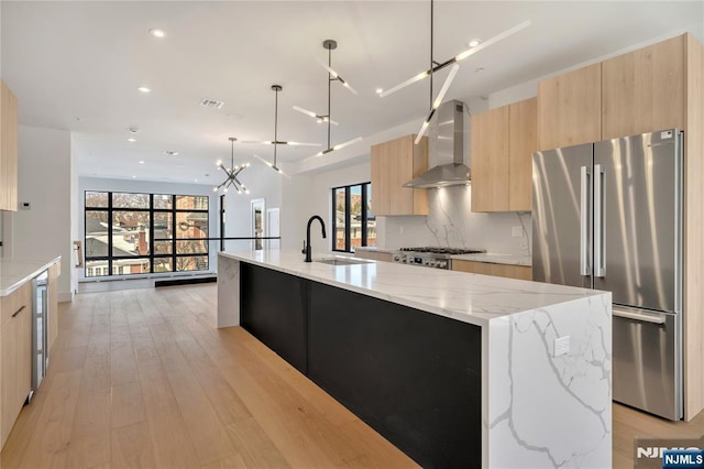 kitchen with wall chimney exhaust hood, light brown cabinetry, a sink, freestanding refrigerator, and modern cabinets