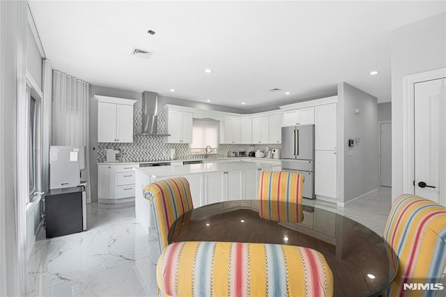 kitchen with high end refrigerator, marble finish floor, backsplash, and wall chimney range hood