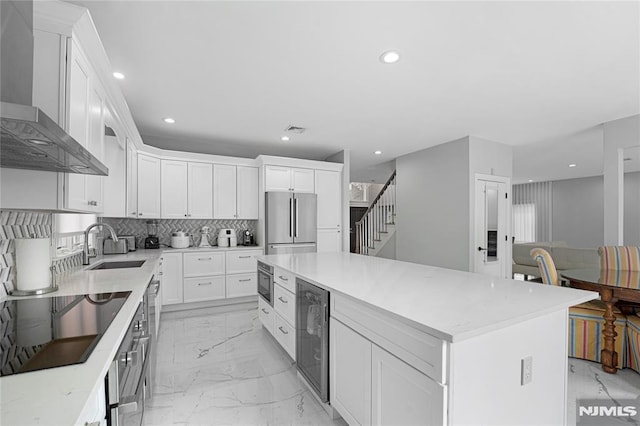 kitchen featuring marble finish floor, beverage cooler, wall chimney range hood, a sink, and appliances with stainless steel finishes