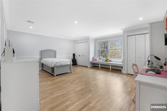 bedroom featuring multiple closets, ornamental molding, light wood-style flooring, and visible vents