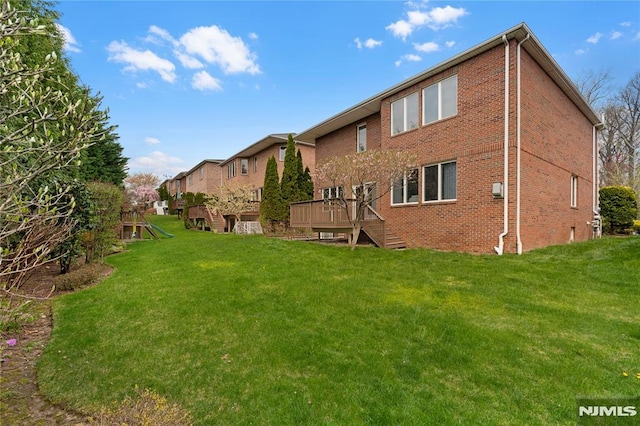 rear view of house featuring a wooden deck, stairs, brick siding, a playground, and a lawn