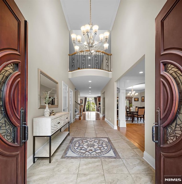 entryway featuring crown molding, baseboards, a high ceiling, and a notable chandelier