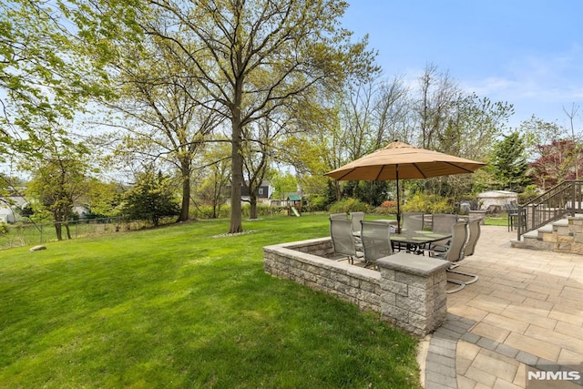 view of property's community featuring fence, outdoor dining space, a patio area, a playground, and a lawn