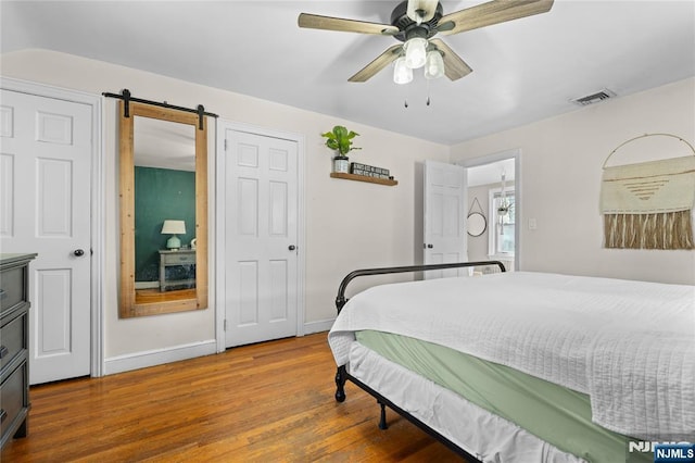 bedroom featuring a barn door, a ceiling fan, wood finished floors, baseboards, and visible vents