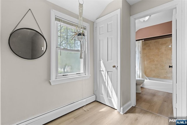 interior space featuring a baseboard radiator, vaulted ceiling, wood finished floors, shower / tub combo, and toilet
