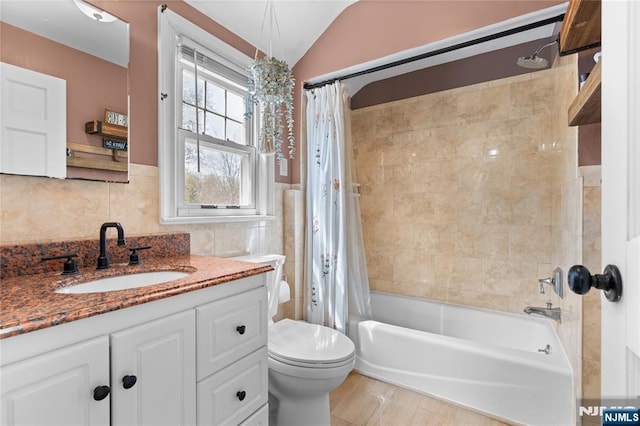 bathroom featuring vaulted ceiling, vanity, tile walls, shower / bath combination with curtain, and toilet