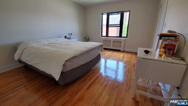 bedroom with radiator heating unit, baseboards, and light wood-style flooring