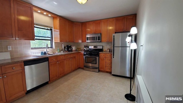 kitchen featuring backsplash, appliances with stainless steel finishes, brown cabinetry, and a sink