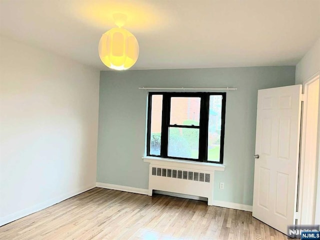 unfurnished room with radiator heating unit, wood finished floors, and baseboards