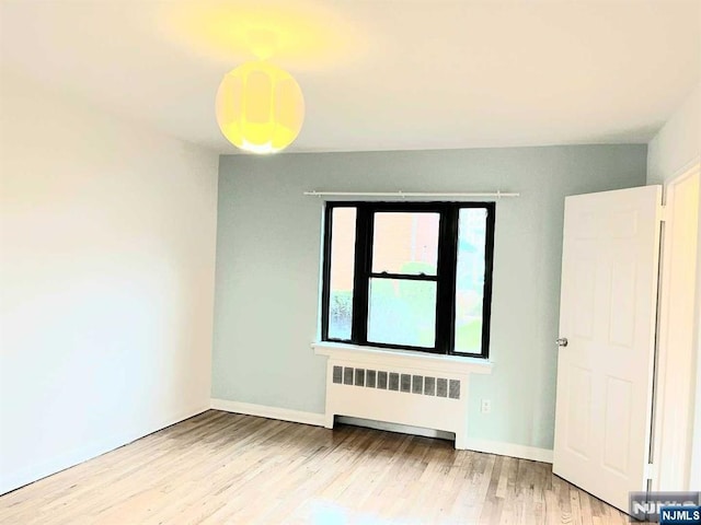 unfurnished room featuring radiator, wood finished floors, and baseboards