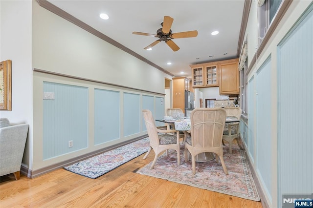 dining room with ornamental molding, light wood-style floors, a decorative wall, wainscoting, and ceiling fan