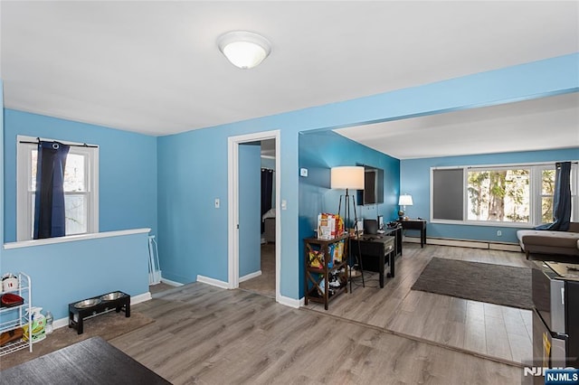 living room with a baseboard heating unit, baseboards, wood finished floors, and plenty of natural light