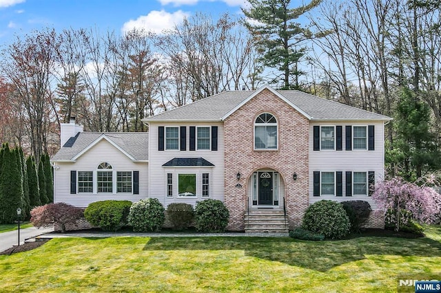 colonial home with a shingled roof, a chimney, and a front yard