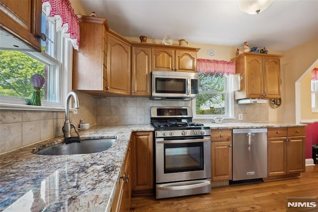 kitchen featuring a sink, stainless steel appliances, light wood-style flooring, backsplash, and light stone countertops