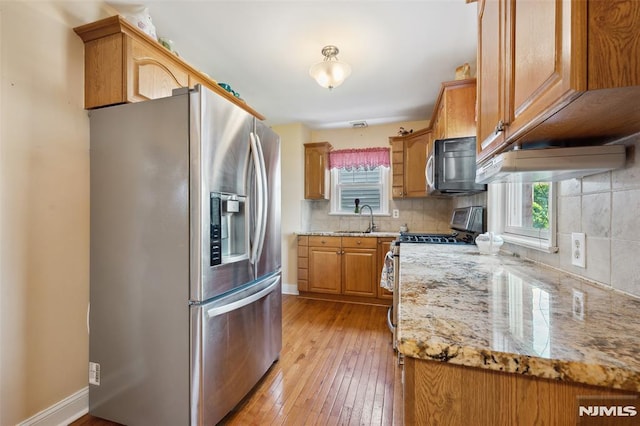 kitchen with a sink, stainless steel appliances, light wood-style flooring, backsplash, and light stone countertops