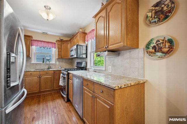 kitchen with light stone counters, stainless steel appliances, a sink, decorative backsplash, and brown cabinetry