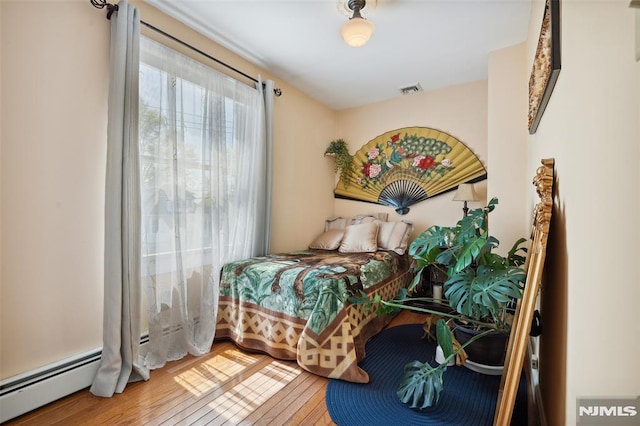 bedroom featuring baseboard heating, wood-type flooring, and visible vents