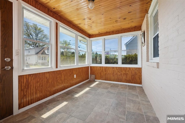 unfurnished sunroom with wood ceiling, baseboards, wood walls, and stone finish floor