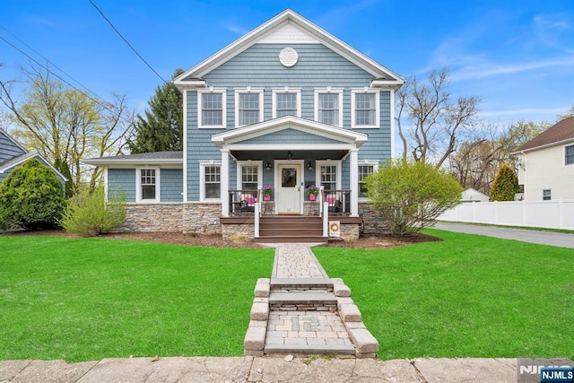 traditional-style house featuring fence, covered porch, a front lawn, and stone siding