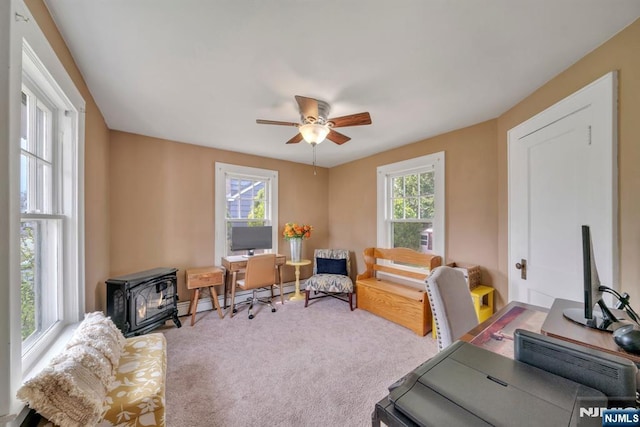 carpeted office space with a wood stove, ceiling fan, and a baseboard radiator