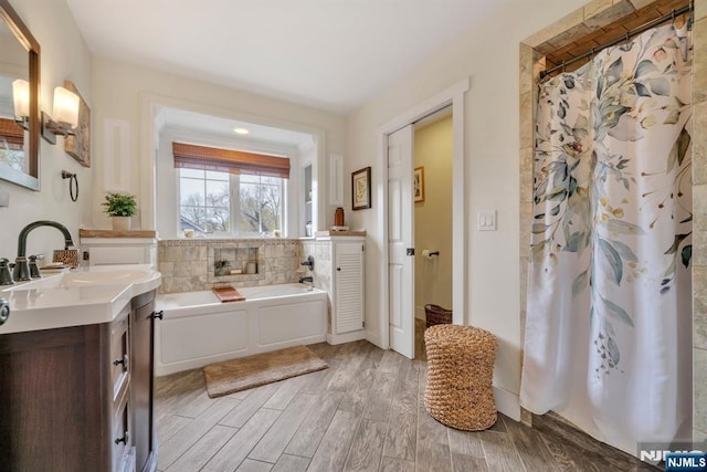 bathroom featuring wood finished floors, a garden tub, a shower with shower curtain, and vanity
