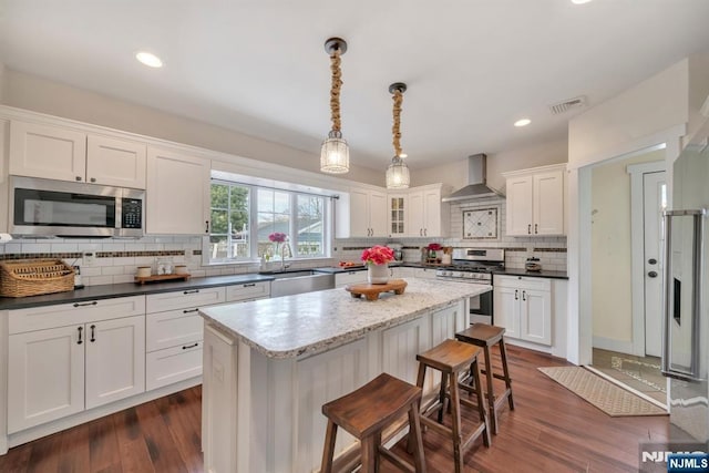 kitchen featuring a sink, stainless steel appliances, wall chimney exhaust hood, visible vents, and white cabinetry