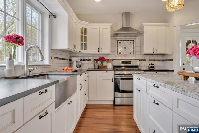 kitchen with wall chimney exhaust hood, stainless steel gas range, a sink, and white cabinetry