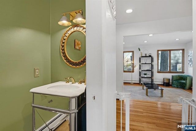 bathroom with recessed lighting, wood finished floors, a baseboard radiator, and a sink