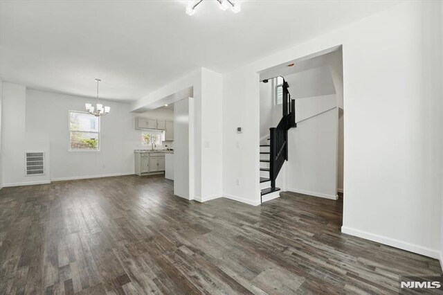 unfurnished living room featuring dark wood finished floors, baseboards, stairs, and a notable chandelier