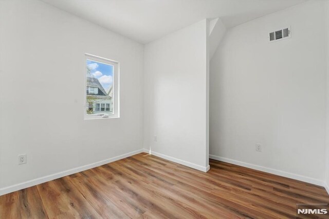 unfurnished room with baseboards, wood finished floors, and visible vents