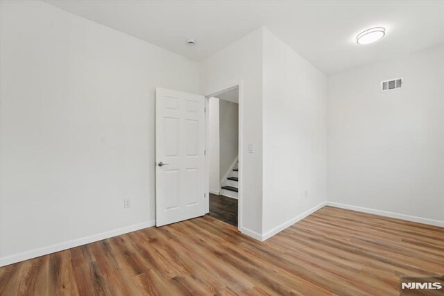 empty room with wood finished floors, visible vents, and baseboards
