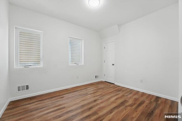 unfurnished room with wood finished floors, visible vents, and baseboards