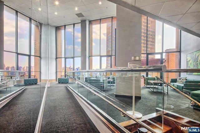 common area featuring floor to ceiling windows, a high ceiling, a view of city, and a paneled ceiling