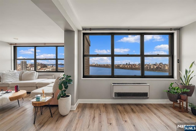sitting room featuring wood finished floors, baseboards, heating unit, a water view, and a view of city