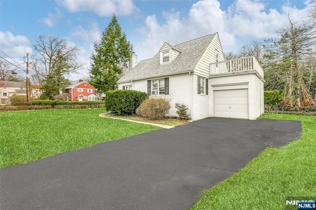 view of side of home with a balcony, driveway, an attached garage, a yard, and brick siding