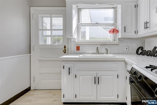 kitchen featuring tile counters, black gas range, a sink, and white cabinetry