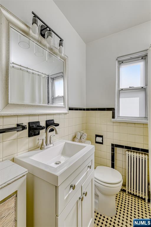 full bath with a wainscoted wall, toilet, tile walls, radiator, and vanity