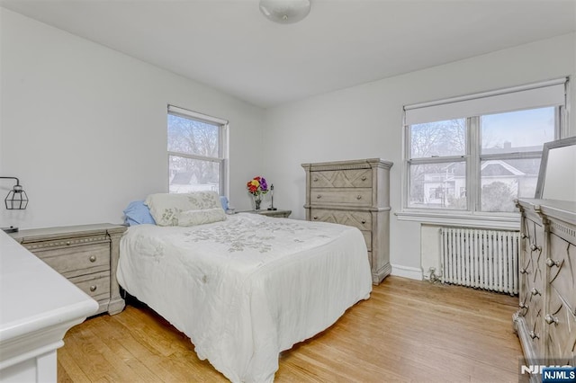 bedroom with radiator, light wood finished floors, and baseboards