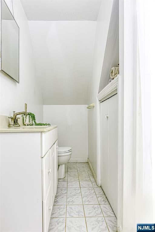 bathroom featuring vaulted ceiling, marble finish floor, vanity, and toilet