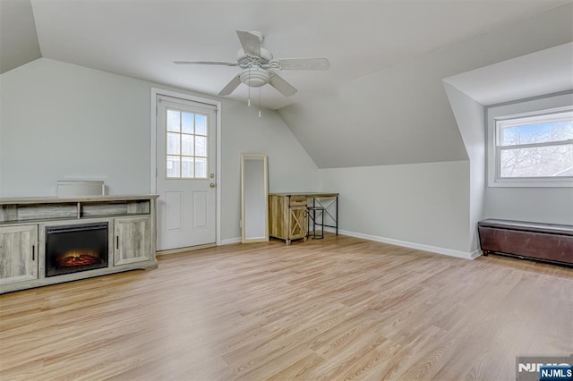 additional living space featuring vaulted ceiling, wood finished floors, a warm lit fireplace, ceiling fan, and baseboards