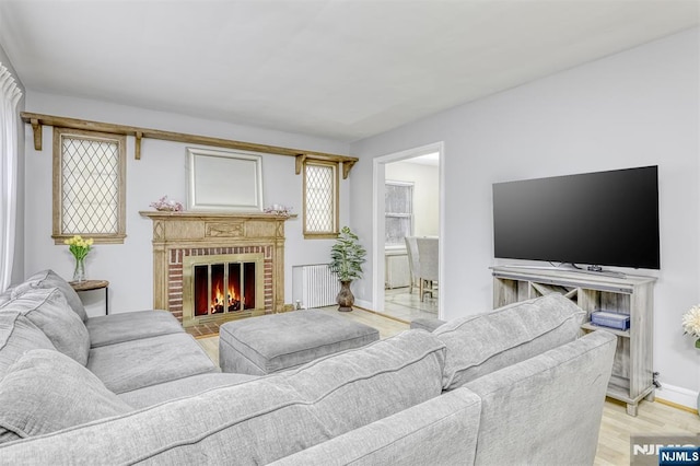 living room with baseboards, radiator heating unit, a brick fireplace, and light wood-style floors
