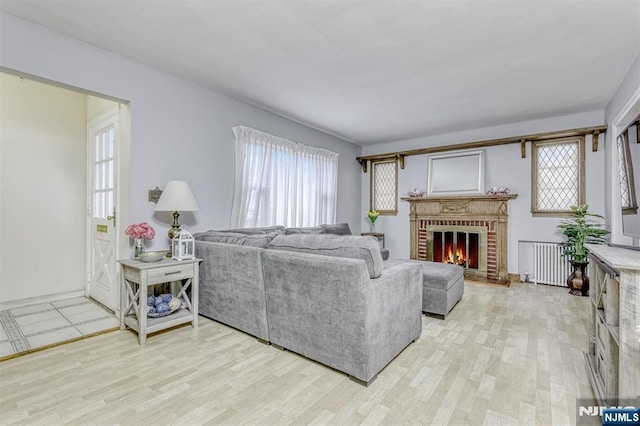 living area featuring a brick fireplace, light wood-style floors, and radiator